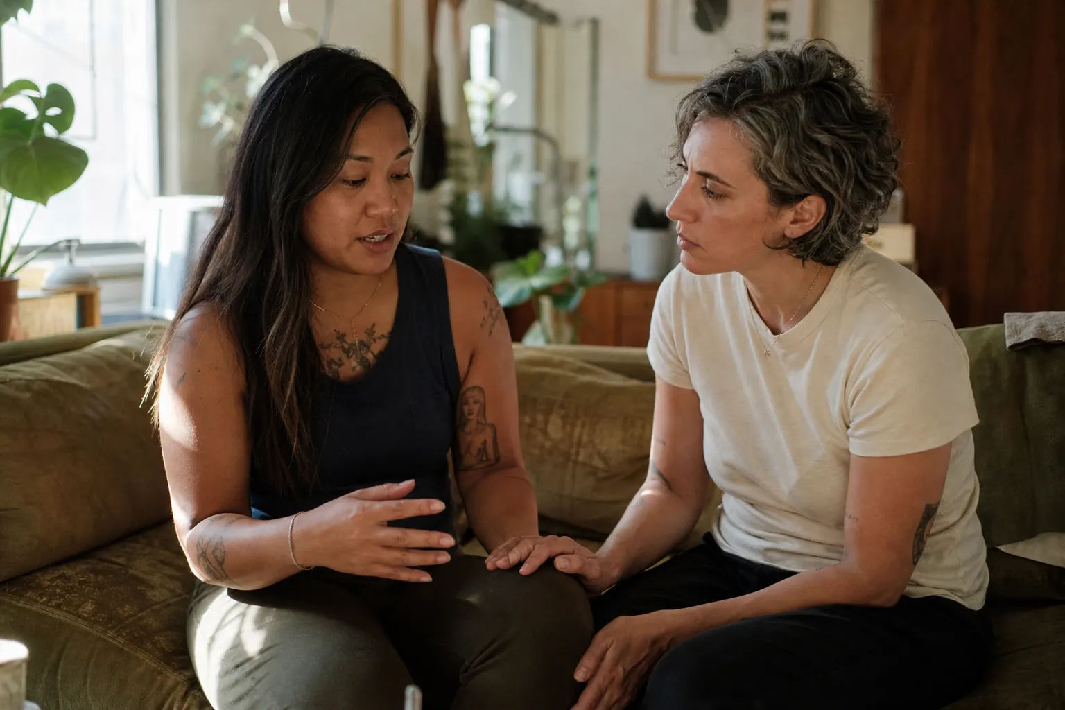 Two women talking quietly on a couch in a sunlit living room